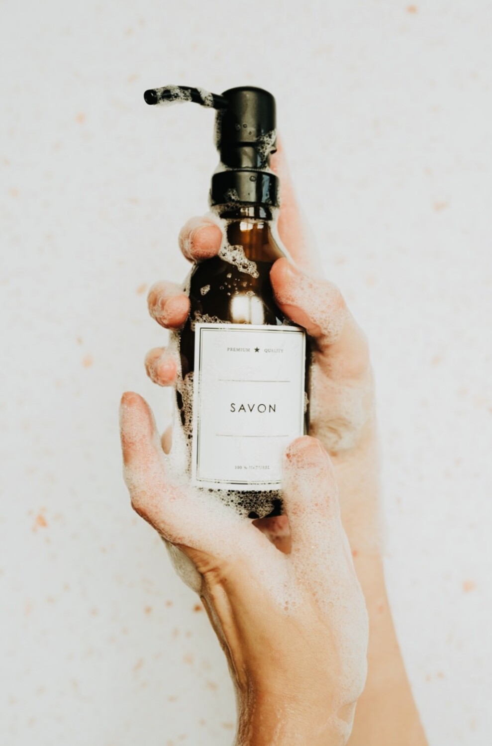 Mains avec mousse de savon tenant le flacon de l'apothicaire pour stocker du savon liquide dans un contenant en verre couleur ambre